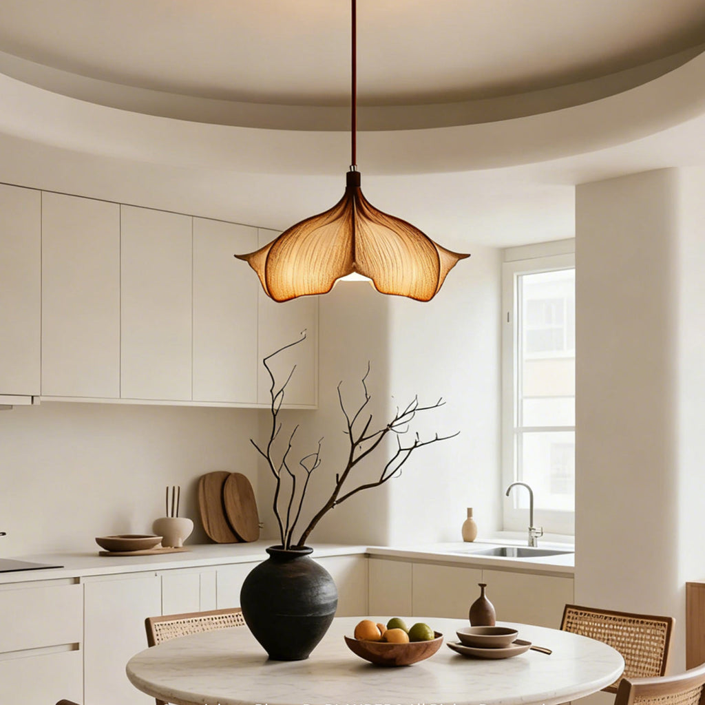 A Clérachic pendant lit above a kitchen table with a black vase of bare branches and a bowl of fruit.