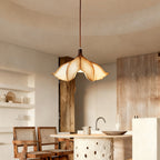 A Clérachic petal-shaped pendant above a kitchen island with rattan chairs and a rough timber post at one side.