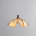 A Clérachic pendant light lit on a grey backdrop, its petal shade glowing amber and cream.