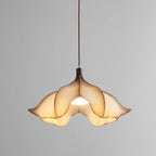 Clérachic pendant on a grey backdrop, lit, with the light showing through the folds of the cream petal shade.