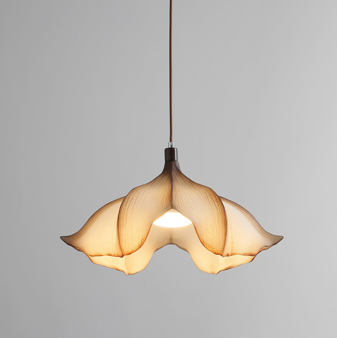 Clérachic pendant on a grey backdrop, lit, with the light showing through the folds of the cream petal shade.