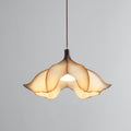 A Clérachic pendant light lit on a grey backdrop, with the bulb visible through the opening between the petals.