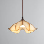 A Clérachic pendant light lit on a grey backdrop, with the bulb visible through the opening between the petals.