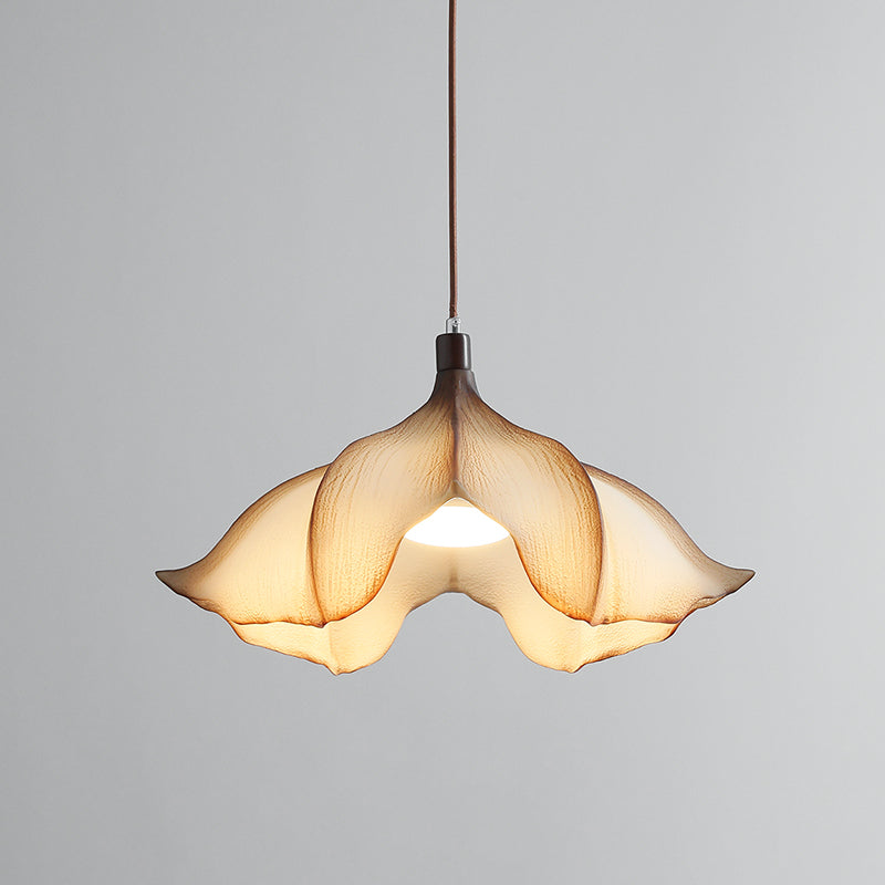 A Clérachic pendant light lit on a grey backdrop, with the bulb visible through the opening between the petals.