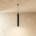Clérachic slim black concrete cylinder pendant light hanging from a black canopy against warm limewash plaster.