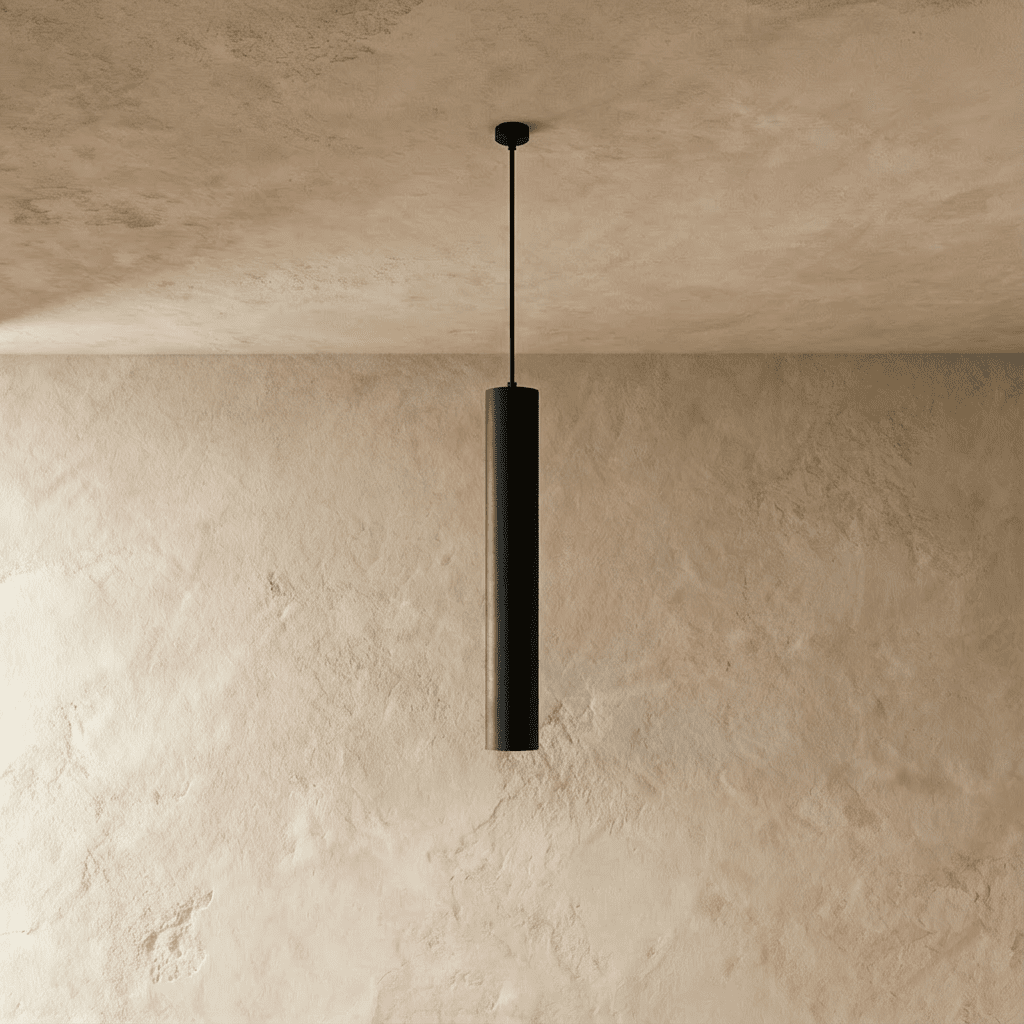 Clérachic slim black concrete cylinder pendant light, switched off, hanging from a thin black stem against textured plaster.
