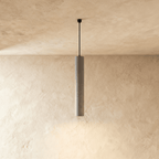 Clérachic slim grey concrete cylinder pendant light with a speckled finish, hung from a black canopy on a plaster wall.