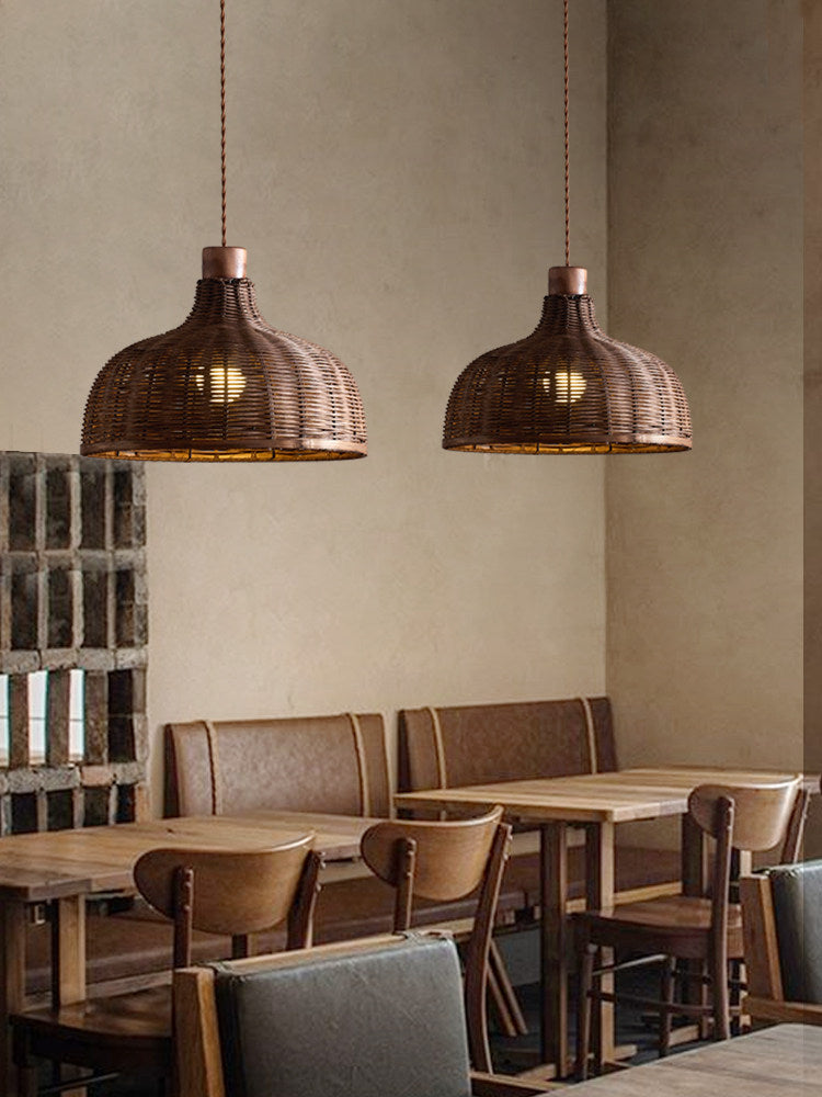Two woven rattan pendants from this Clérachic fixture hang above wooden booth seating in a dining room.