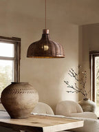 A woven rattan pendant from this Clérachic fixture lights a rustic table beside a large ceramic vessel.