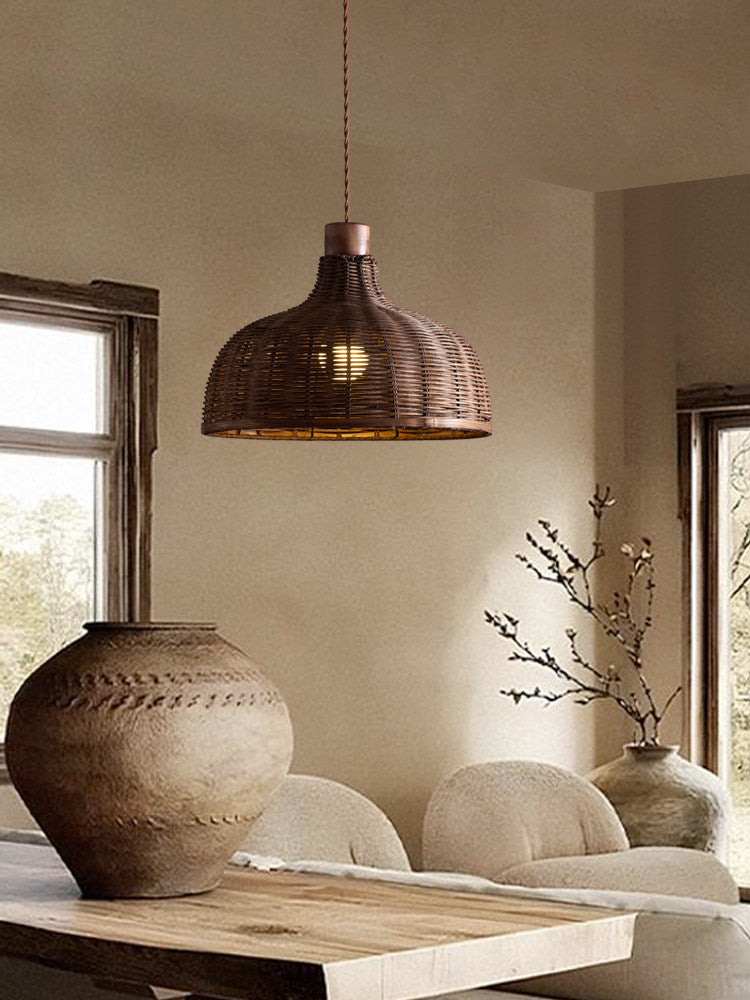 A woven rattan pendant from this Clérachic fixture lights a rustic table beside a large ceramic vessel.