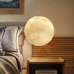 Lit glowing sphere from Clérachic beside a bed with a slatted wood headboard, soft light picking out the crater-like surface.