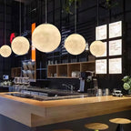Five Clérachic globe pendants graduate in size above a wooden bar counter, glowing warmly against a dark tiled wall.