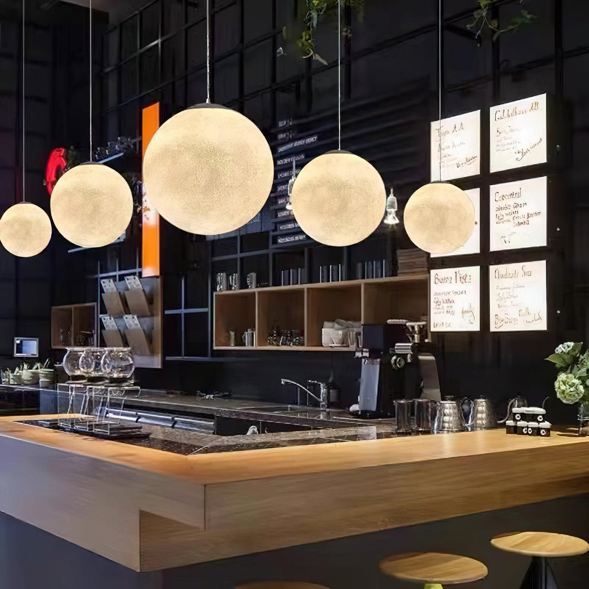 Five Clérachic globe pendants graduate in size above a wooden bar counter, glowing warmly against a dark tiled wall.