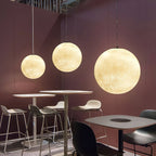 Three lit Clérachic spheres of rising size hang over high stools and café tables in a room with plum-coloured walls.
