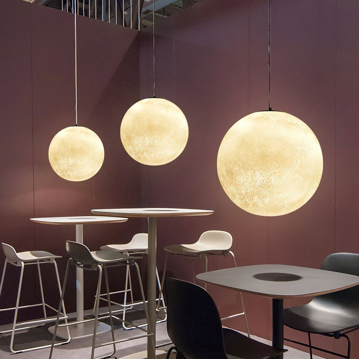 Three lit Clérachic spheres of rising size hang over high stools and café tables in a room with plum-coloured walls.