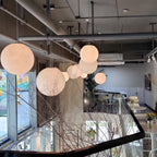 Pale pink-white Clérachic spheres cluster at different heights beneath an exposed industrial ceiling in a bright, open café.