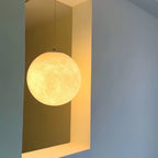 Seen against a pale blue wall, this Clérachic sphere glows golden in a recessed yellow niche, hung from a slim grey cord.