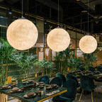 Three large Clérachic spheres in warm white hang over dining tables set among palms and green velvet chairs.