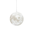 Front view of a cratered moon-print globe pendant from Clérachic, hung on a thin cord and lit softly from within against white.