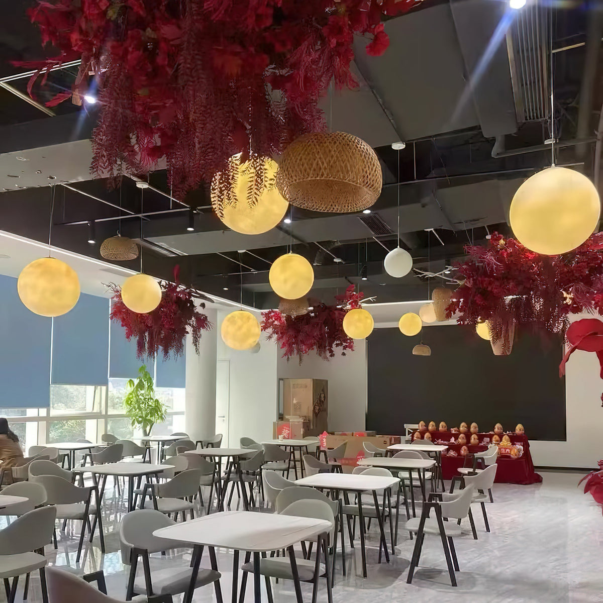 Warm-lit Clérachic spheres float at different heights above white café tables, among red floral decorations and a woven rattan shade.
