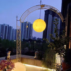 A glowing yellow Clérachic sphere hangs from a decorative metal arch at dusk, with city towers behind it.