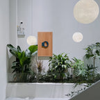 Three white Clérachic spheres of rising size hang above a planted white stair void, beside a small wooden wall panel.