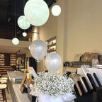 Frosty white Clérachic spheres in two sizes hang above a café counter, with balloons and a bouquet of gypsophila below.
