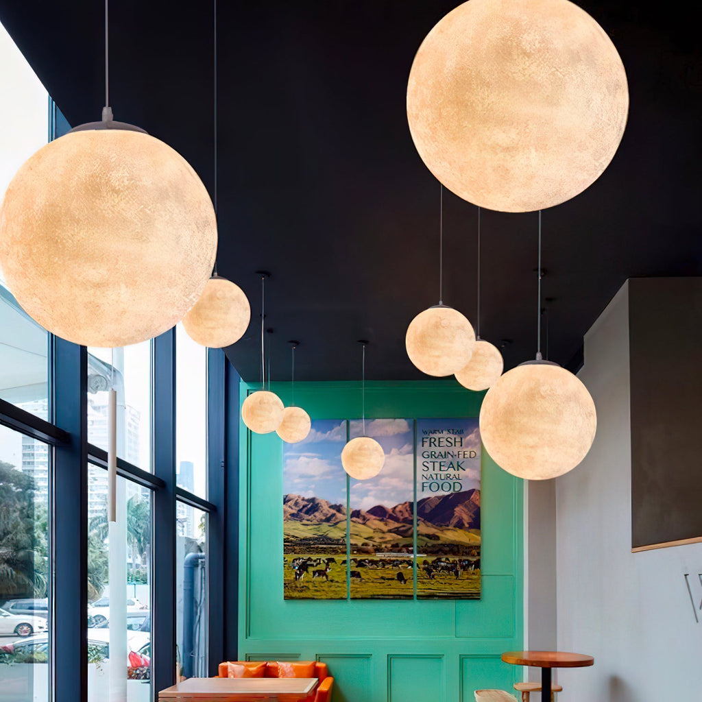 Clérachic spheres of varied sizes hang at different heights, glowing peach-gold in front of tall windows and a teal green wall.