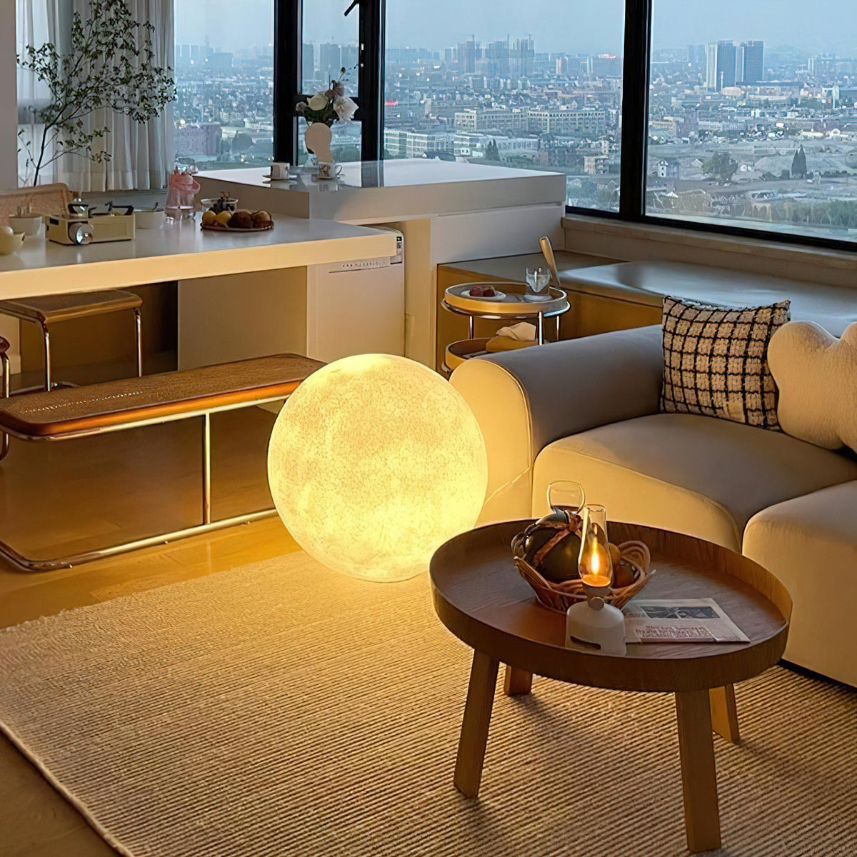 A big lit sphere from Clérachic rests on the floor beside a cream sofa and a round wooden coffee table, with a city view behind.
