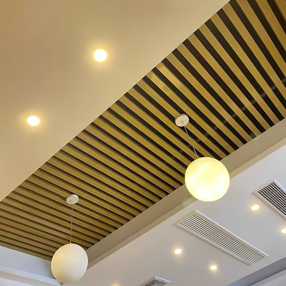 Two Clérachic white spheres hang from short cords beneath a ceiling of slatted wood and recessed spotlights.