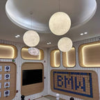 Three lit Clérachic spheres of different sizes hang under a round, domed ceiling with spotlights, over a wall of padded wood panels.