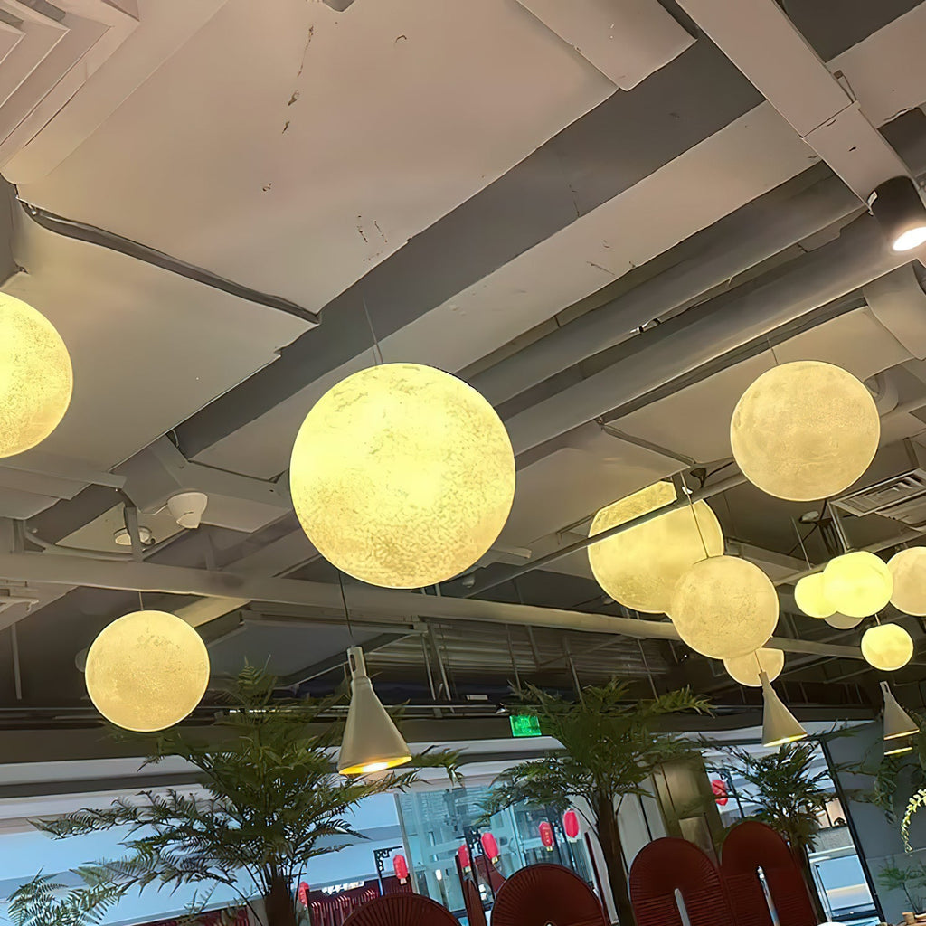 Warm white Clérachic spheres of mixed sizes hang from an exposed concrete ceiling above indoor palms and red chairs.