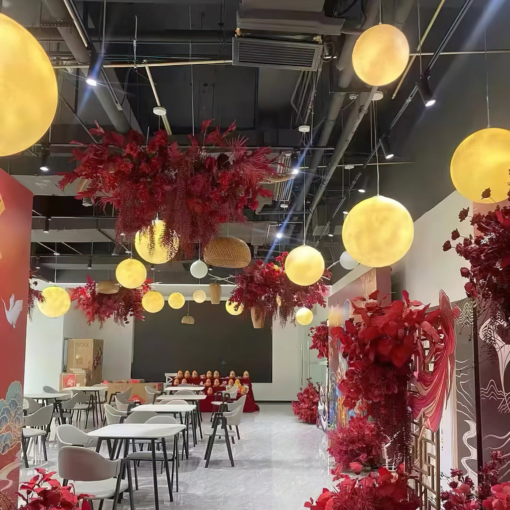 Glowing Clérachic spheres hang at varied heights beneath a black ceiling, among hanging red flowers and white café tables.