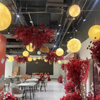 Glowing Clérachic spheres hang at varied heights beneath a black ceiling, among hanging red flowers and white café tables.