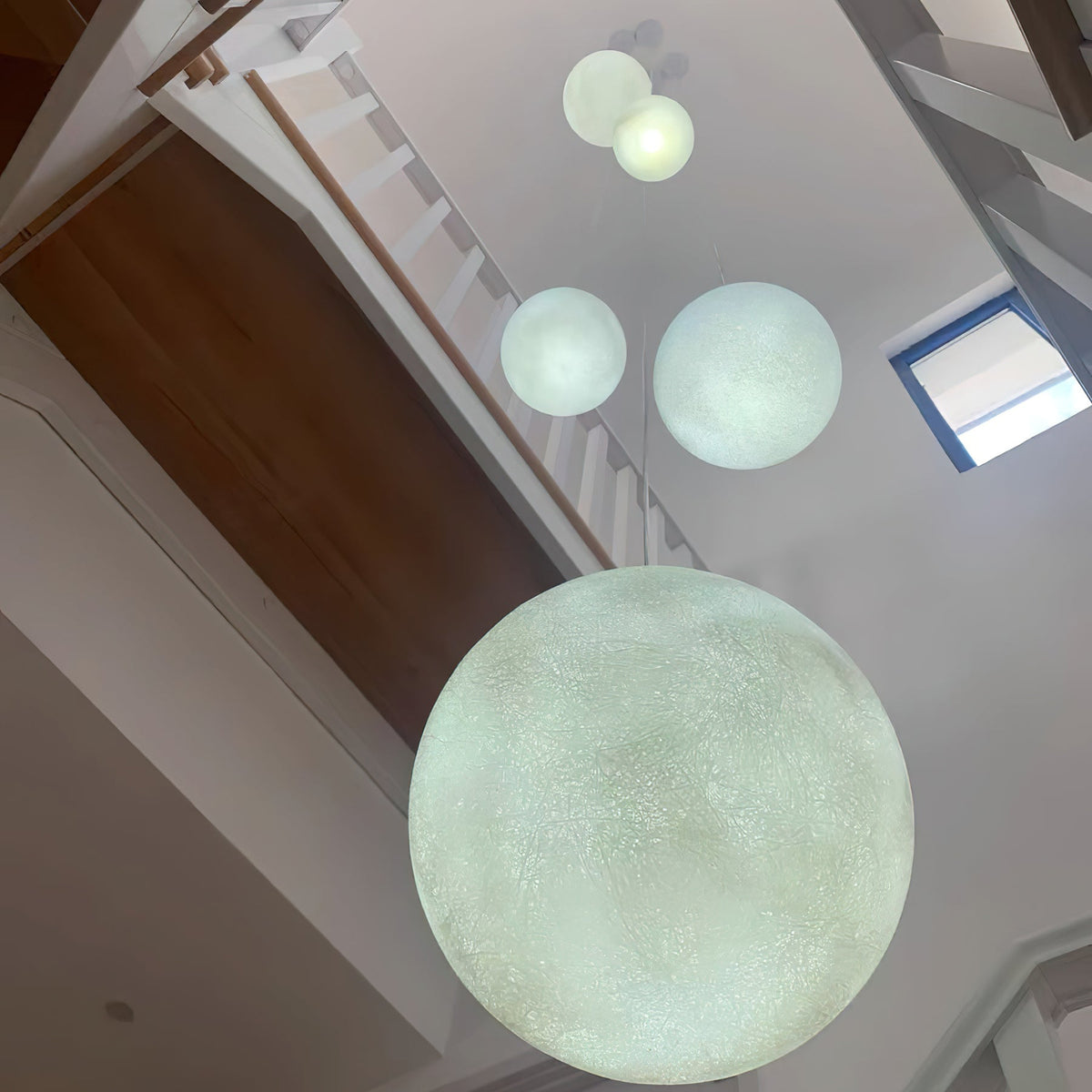 Looking down a stairwell, a large pale green-white Clérachic sphere hangs in the foreground with smaller ones higher up.
