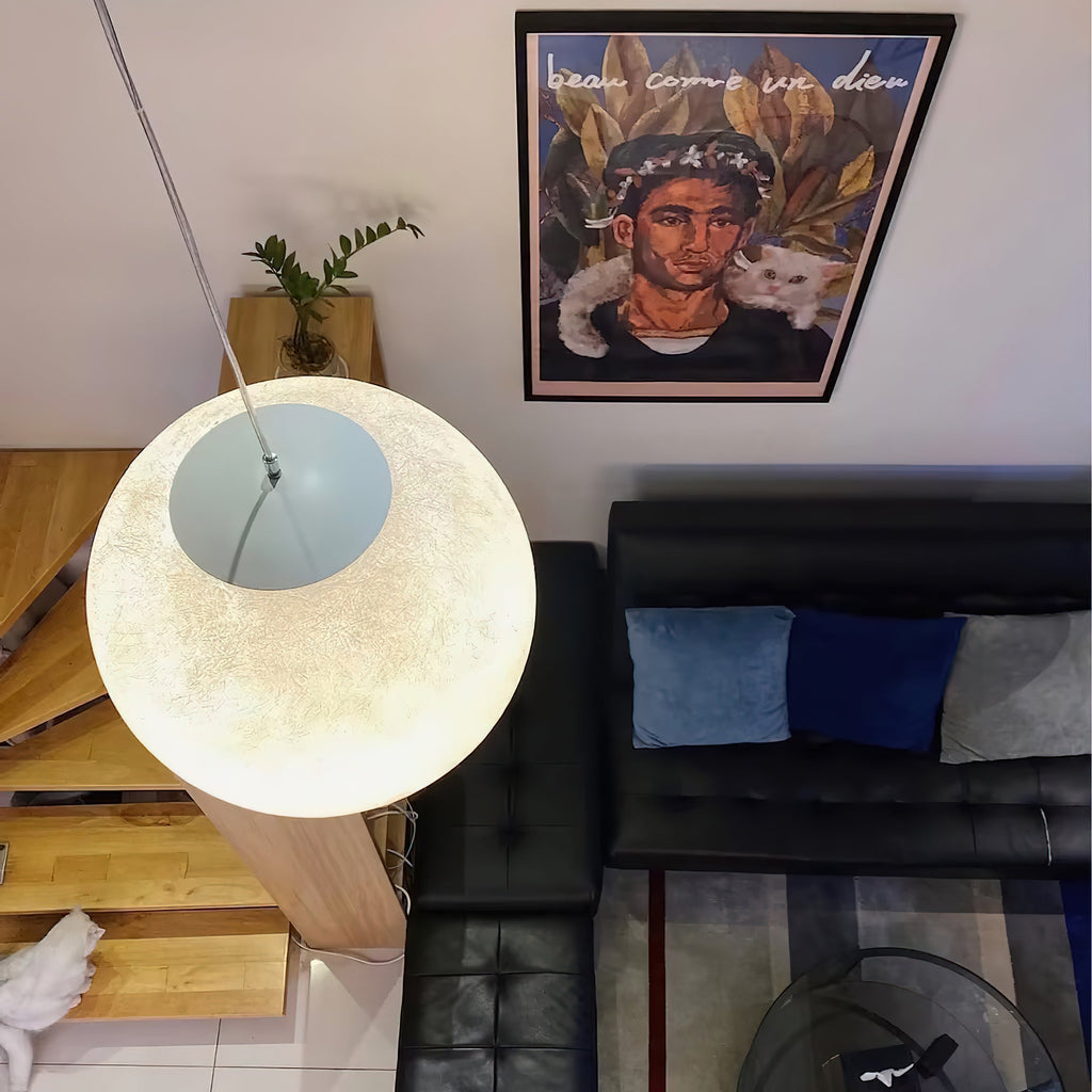 A lit Clérachic sphere seen from above, its white canopy visible, over a black leather sofa and a pine stair.