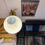 A lit Clérachic sphere seen from above, its white canopy visible, over a black leather sofa and a pine stair.