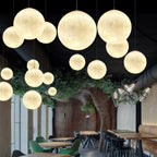 A crowd of Clérachic spheres in warm white hangs at many heights in a restaurant with green chairs and a sculpted tree wall.