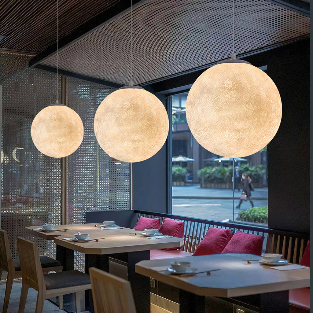 Three Clérachic spheres of rising size hang above wooden dining tables with red cushions, against a perforated metal wall.