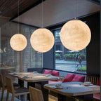 Three Clérachic spheres of rising size hang above wooden dining tables with red cushions, against a perforated metal wall.
