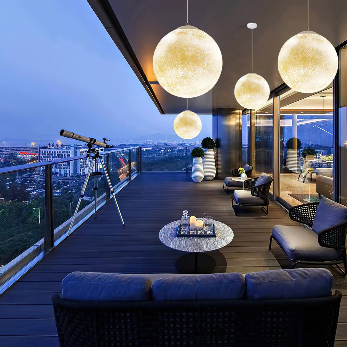 On a deck at dusk, warm Clérachic spheres hang at three heights above outdoor sofas and a round table, with a telescope beyond.
