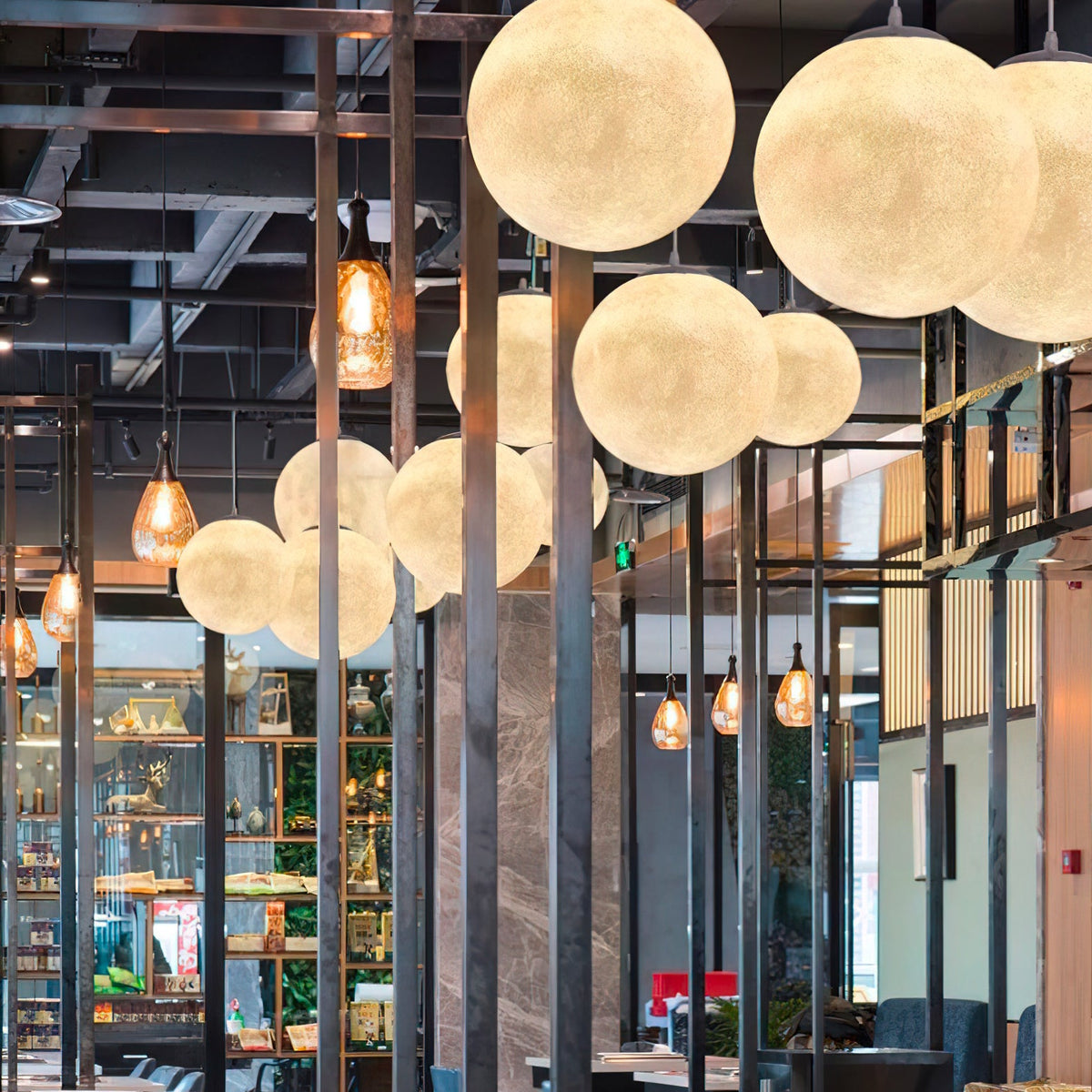 Large Clérachic spheres hang close together in front of dark steel columns, amber filament pendants and shelves of glassware.