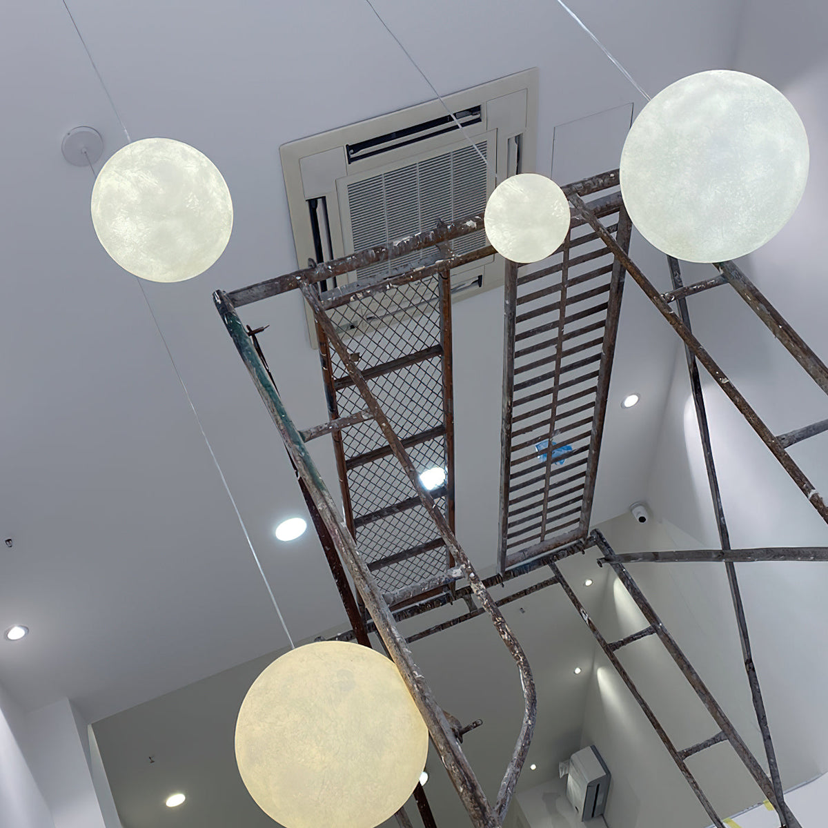 Looking up a stairwell, three pale Clérachic spheres hang at different heights beside a rusted metal staircase.