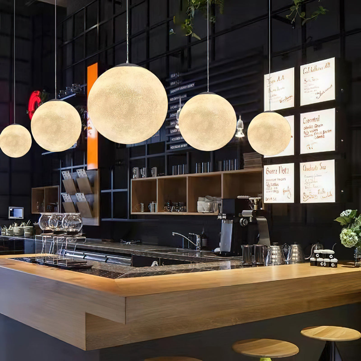 Five Clérachic spheres of graduated size glow over a wooden bar counter with espresso equipment and illuminated menu boards.