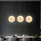 Three evenly spaced Clérachic spheres in warm white hang over a dining table, against a dark slatted wall.