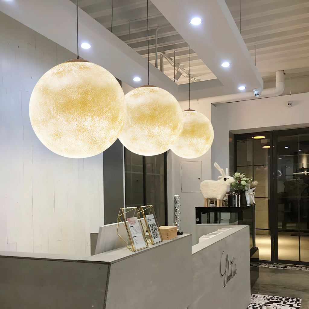 Three Clérachic spheres, lit golden and graduated in size, hang above a grey reception desk in a bright shopfront.