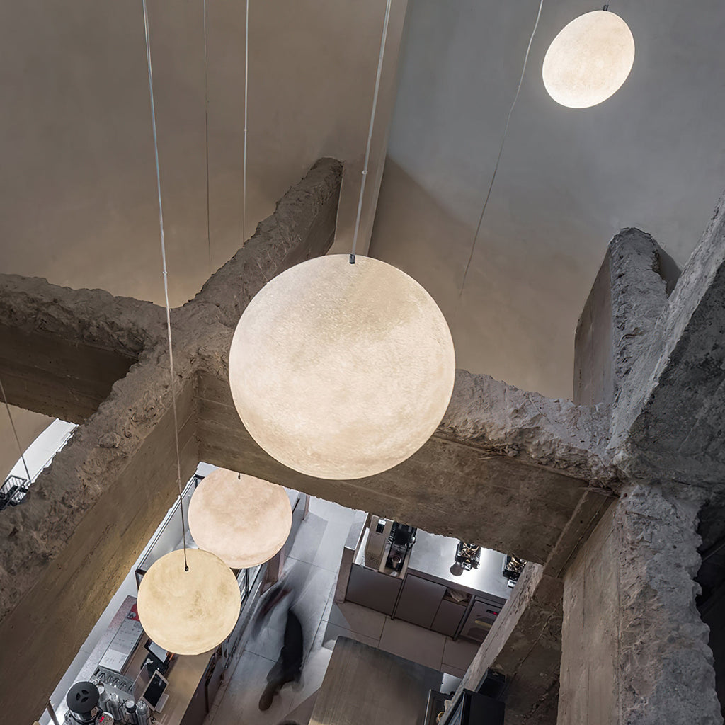 Looking down from a concrete mezzanine, a pale Clérachic sphere hangs in front of rough pillars, with smaller ones below.