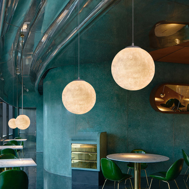Two Clérachic spheres hang at different heights in a teal curved-wall café, above green chairs and a round table.