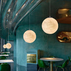 Two Clérachic spheres hang at different heights in a teal curved-wall café, above green chairs and a round table.