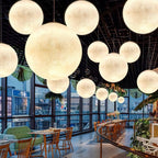 A dense cluster of Clérachic spheres in many sizes hangs under a black ceiling in a glass-walled restaurant.